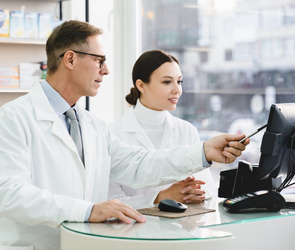 pharmacist pointing showing male colleague medication prices prescriptions on computer screen.jpg